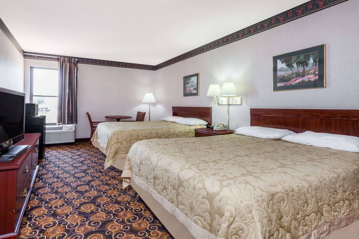 Une chambre d’hôtel avec deux lits, un bureau, une télévision et une fenêtre avec des rideaux.