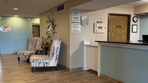 A reception area with a reception desk, two patterned armchairs, a wall clock, and informational posters. - Super 8 by Wyndham Evansville North (Evansville)