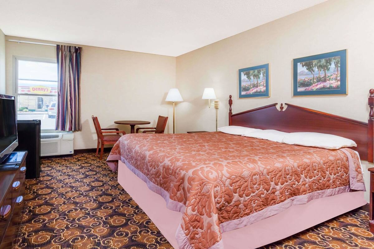 Une chambre d’hôtel avec un grand lit, un bureau, une chaise, une télévision et deux tableaux accrochés au mur.