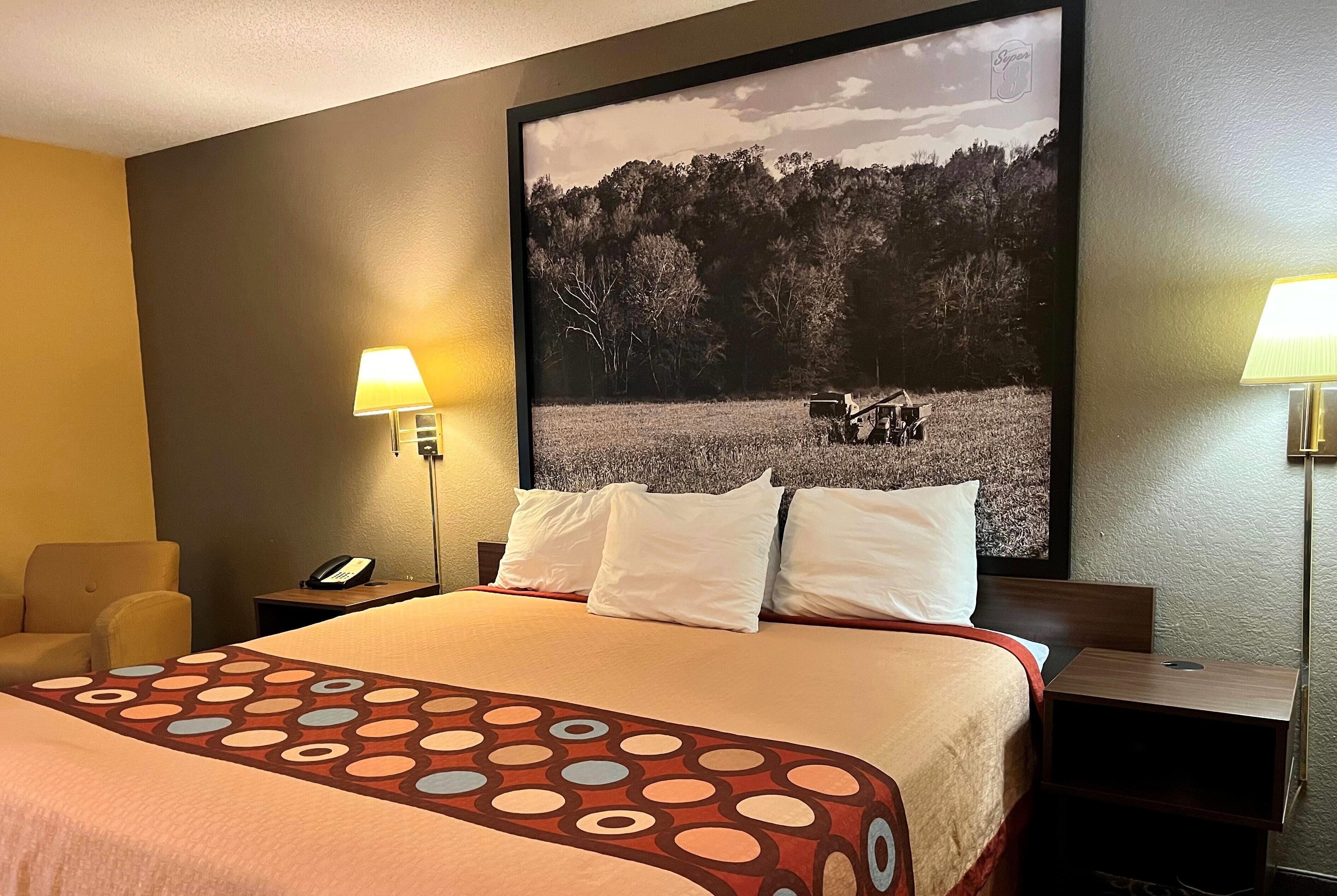 A hotel room with a large bed, two bedside tables, a chair, and a wall-mounted lamp.