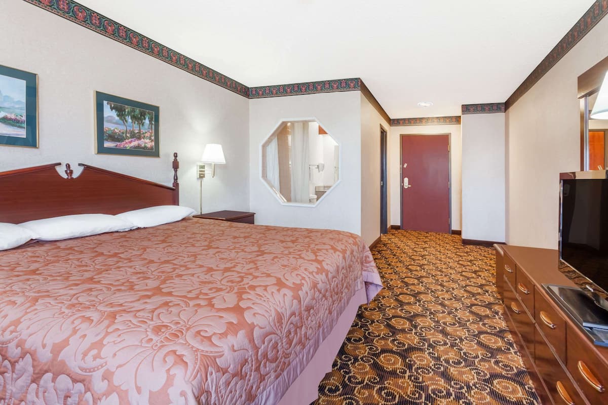 Une chambre d’hôtel avec un grand lit, une télévision, une commode, un miroir et un sol recouvert de moquette.