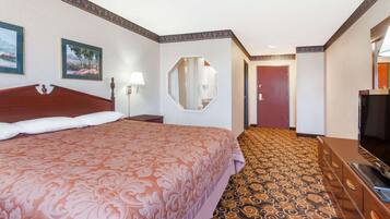A hotel room with a large bed, a television, a dresser, a mirror, and a carpeted floor.