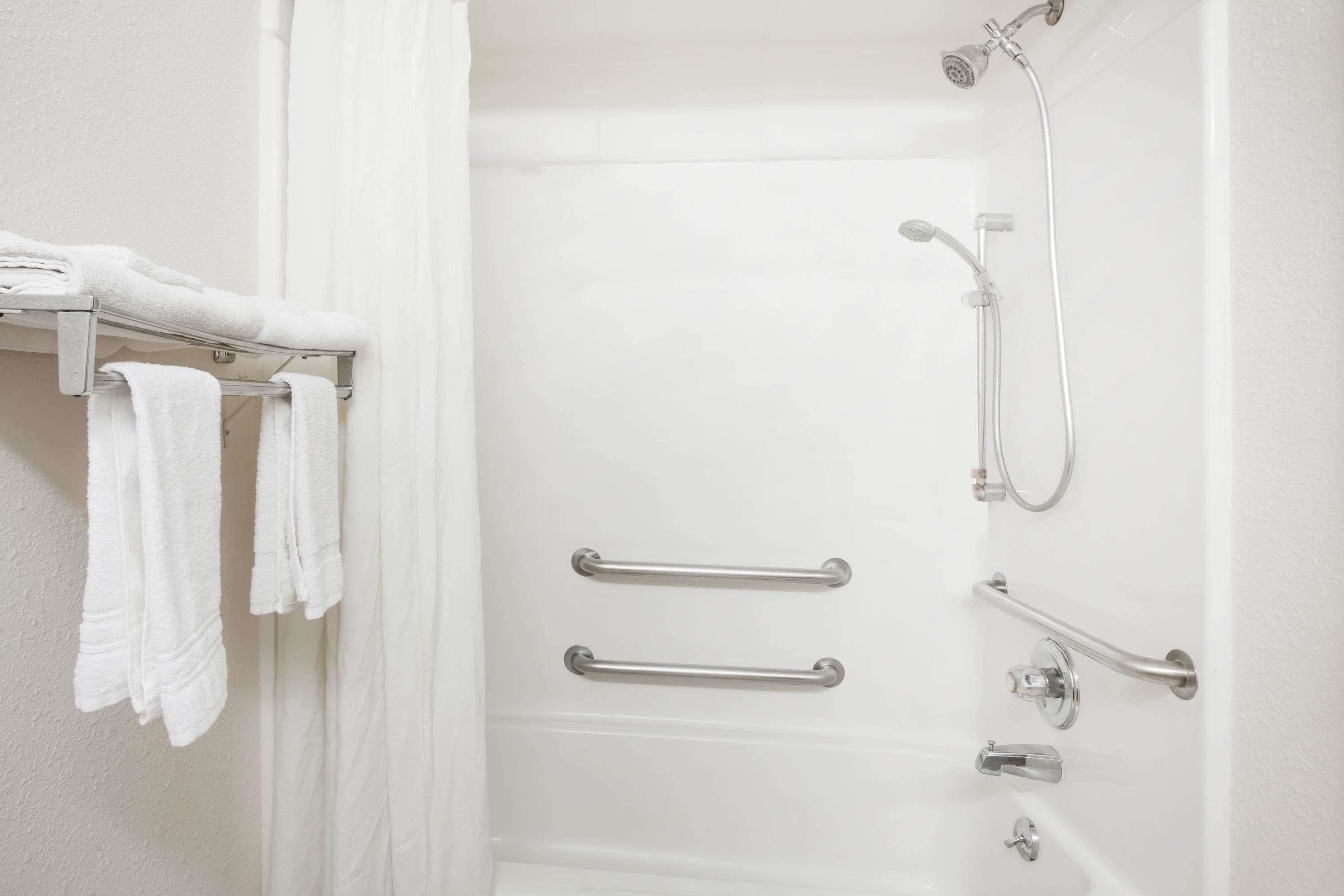 A white bathroom with a shower, grab bars, and a towel rack.