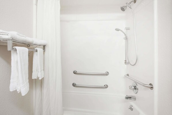 A white bathroom with a shower, grab bars, and a towel rack.