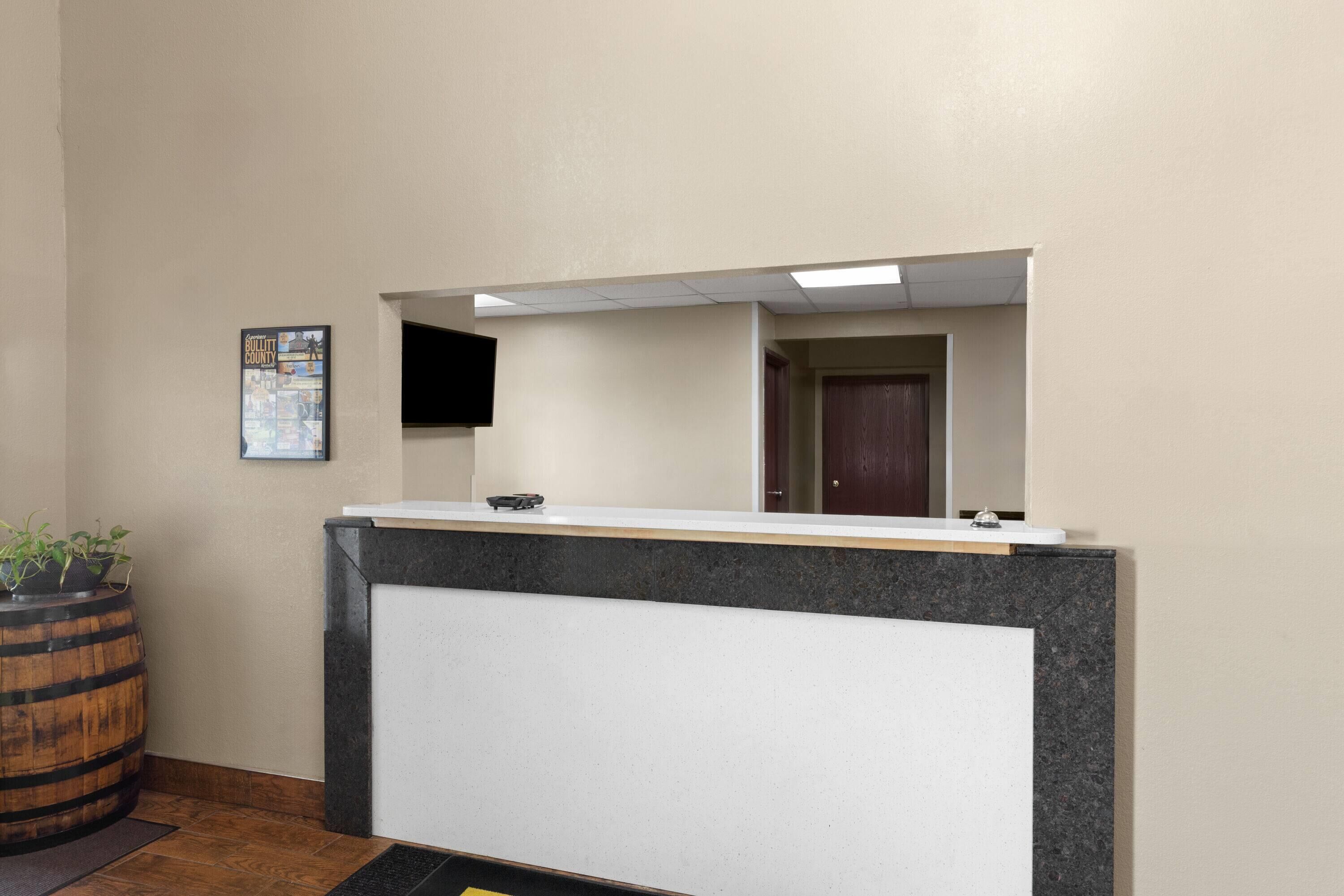 A reception desk with a white counter and a dark marble base, a wooden barrel with plants, and a framed map on the wall.
