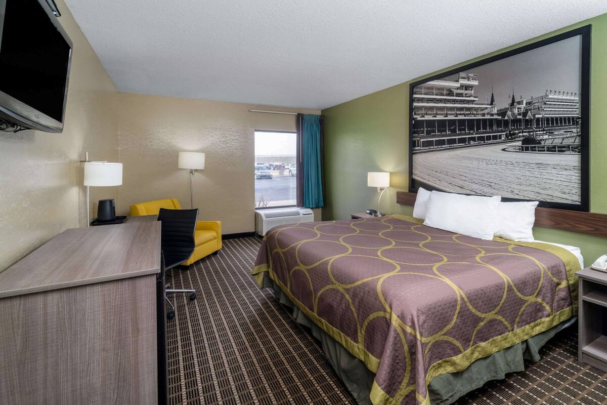 Habitación de hotel con cama, escritorio, silla, dos lámparas, televisión y un ventanal grande.