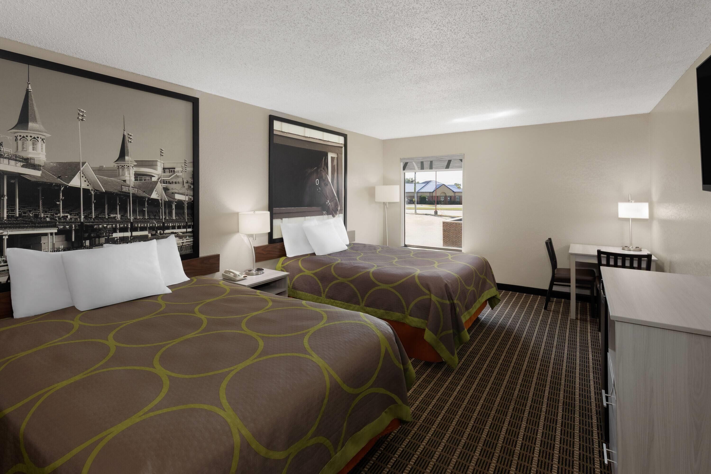 A hotel room with two beds, a desk, a chair, and a large window.