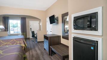 A hotel room with a bed, desk, refrigerator, microwave, TV, and a window with curtains.