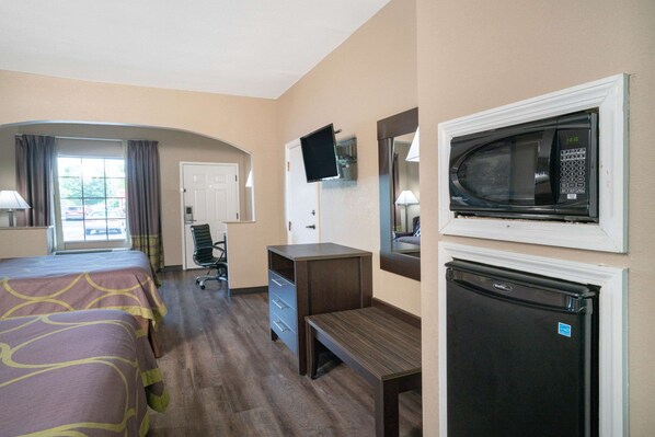A hotel room with a bed, desk, refrigerator, microwave, TV, and a window with curtains.