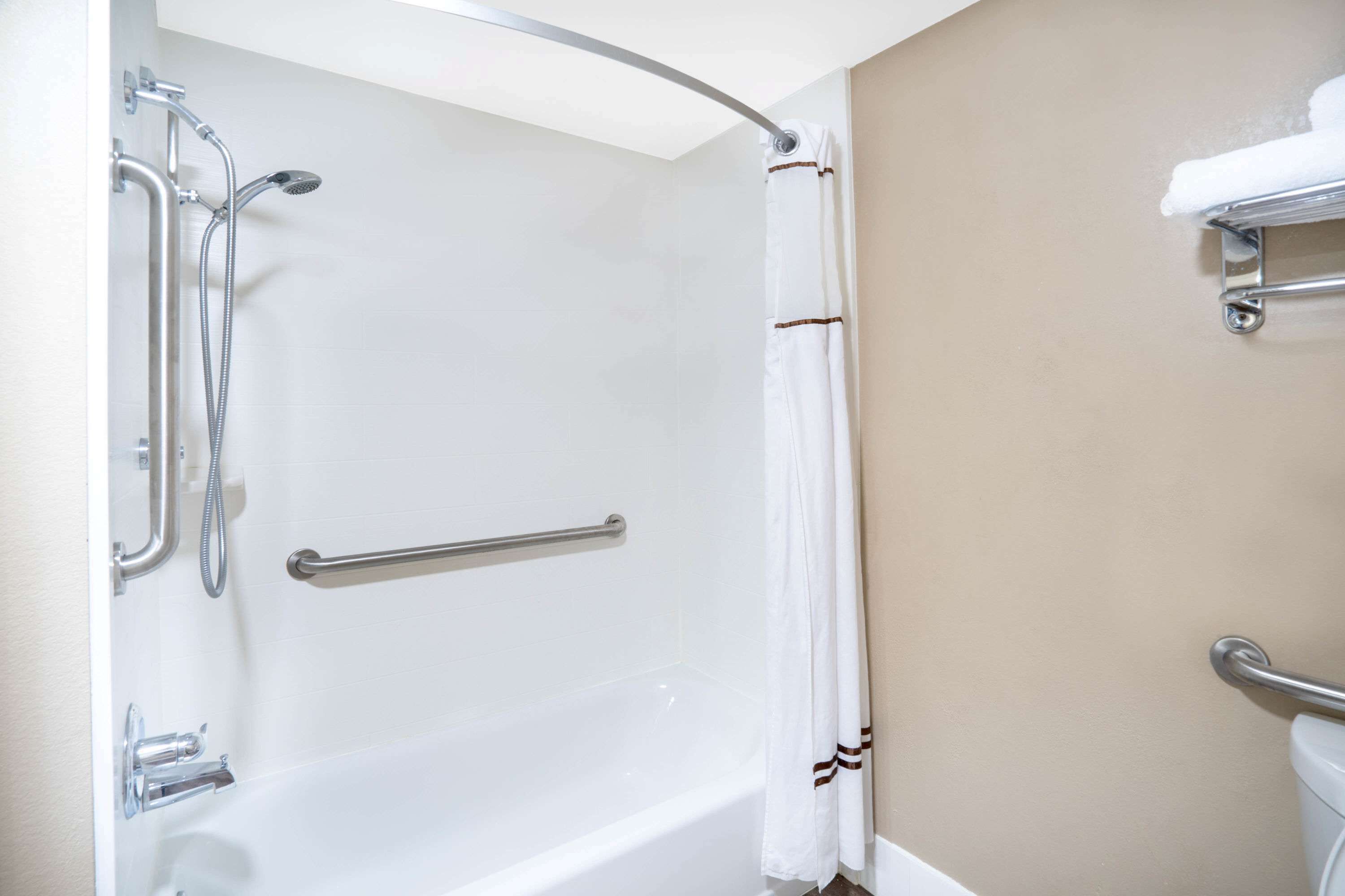 A bathroom with a white bathtub, a shower with a handheld showerhead, and a grab bar.