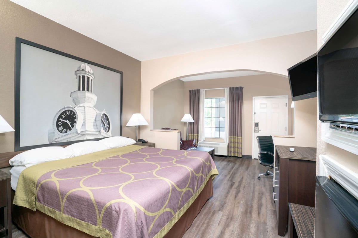A hotel room with a large bed, a desk, a chair, a television, and a clock on the wall.