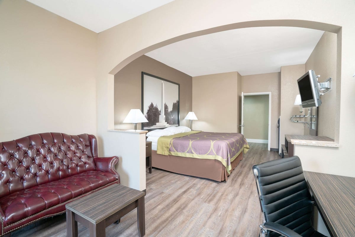 A hotel room with a leather sofa, a bed with a green and purple bedspread, a desk with a computer, and a TV mounted on the wall.