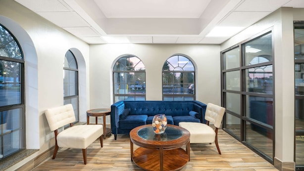 Una habitación amplia con un sofá azul, dos sillones blancos y una mesa de centro de vidrio.