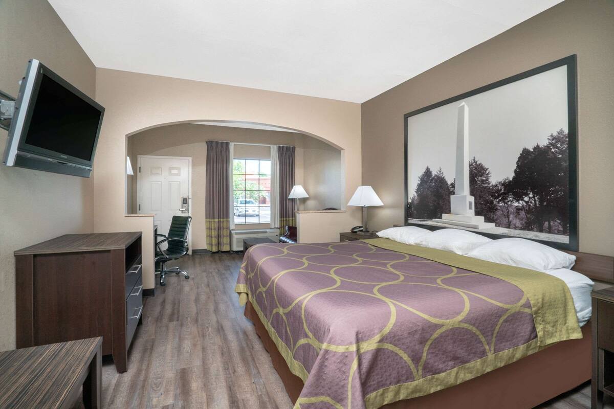 A hotel room with a large bed, a desk, a chair, a TV, and a window with curtains.