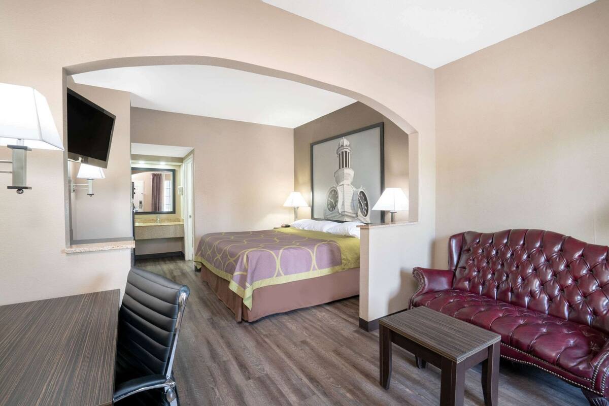 A hotel room with a bed, a leather sofa, a small table, a TV, and a mirror.