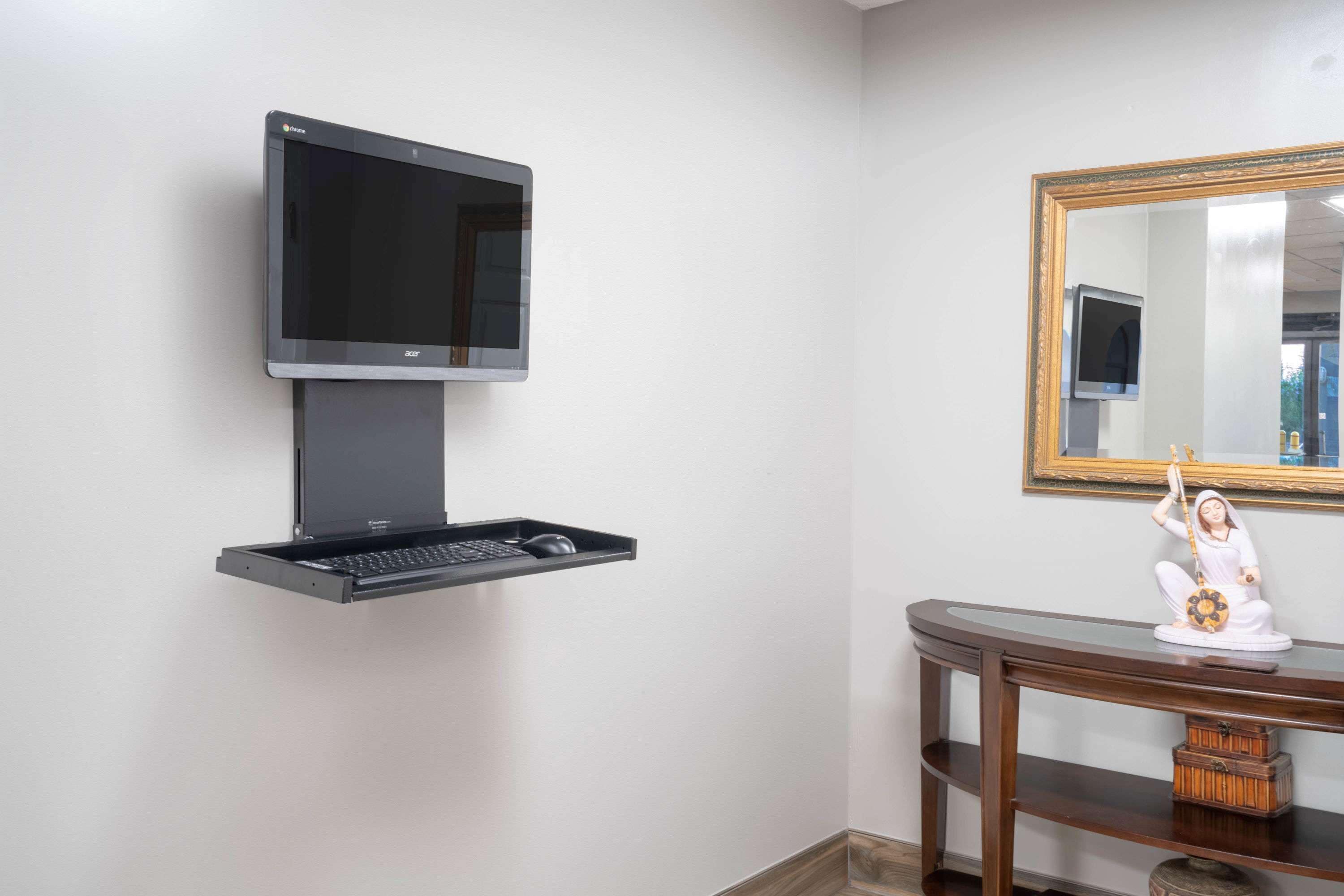 Un televisor montado en la pared con un cajón para teclado debajo, una consola de madera con una estatua, y un espejo con marco dorado.