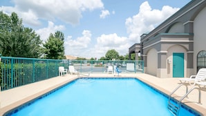 Una piscina con borde azul, rodeada por una valla y sillas reclinables blancas.