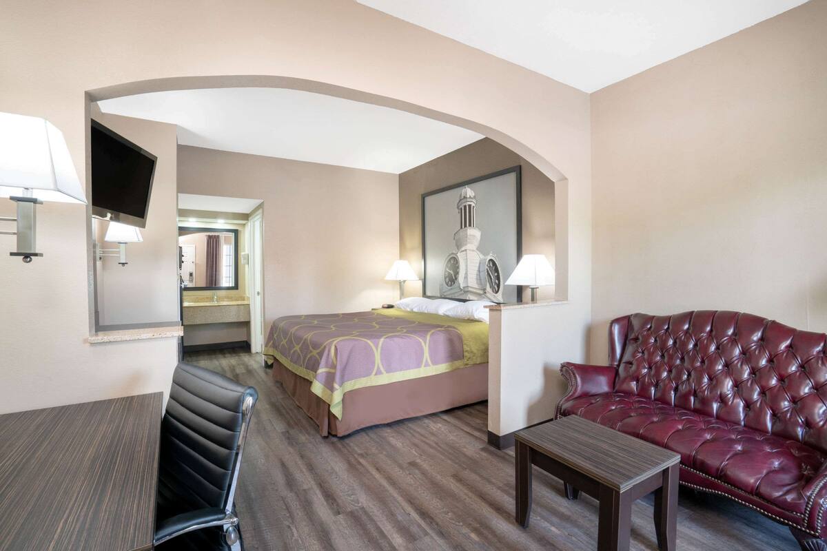 A hotel room with a bed, a red leather sofa, a small table, and a TV mounted on the wall.