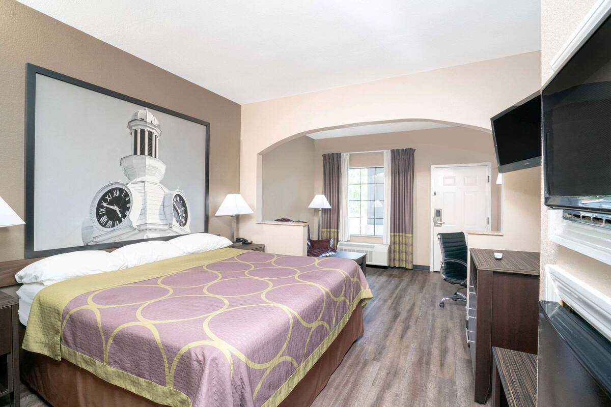 A hotel room with a large bed, a desk, a TV, and a clock on the wall.