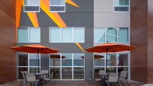 Une terrasse extérieure avec des tables et des chaises, de grandes fenêtres et des parasols orange.