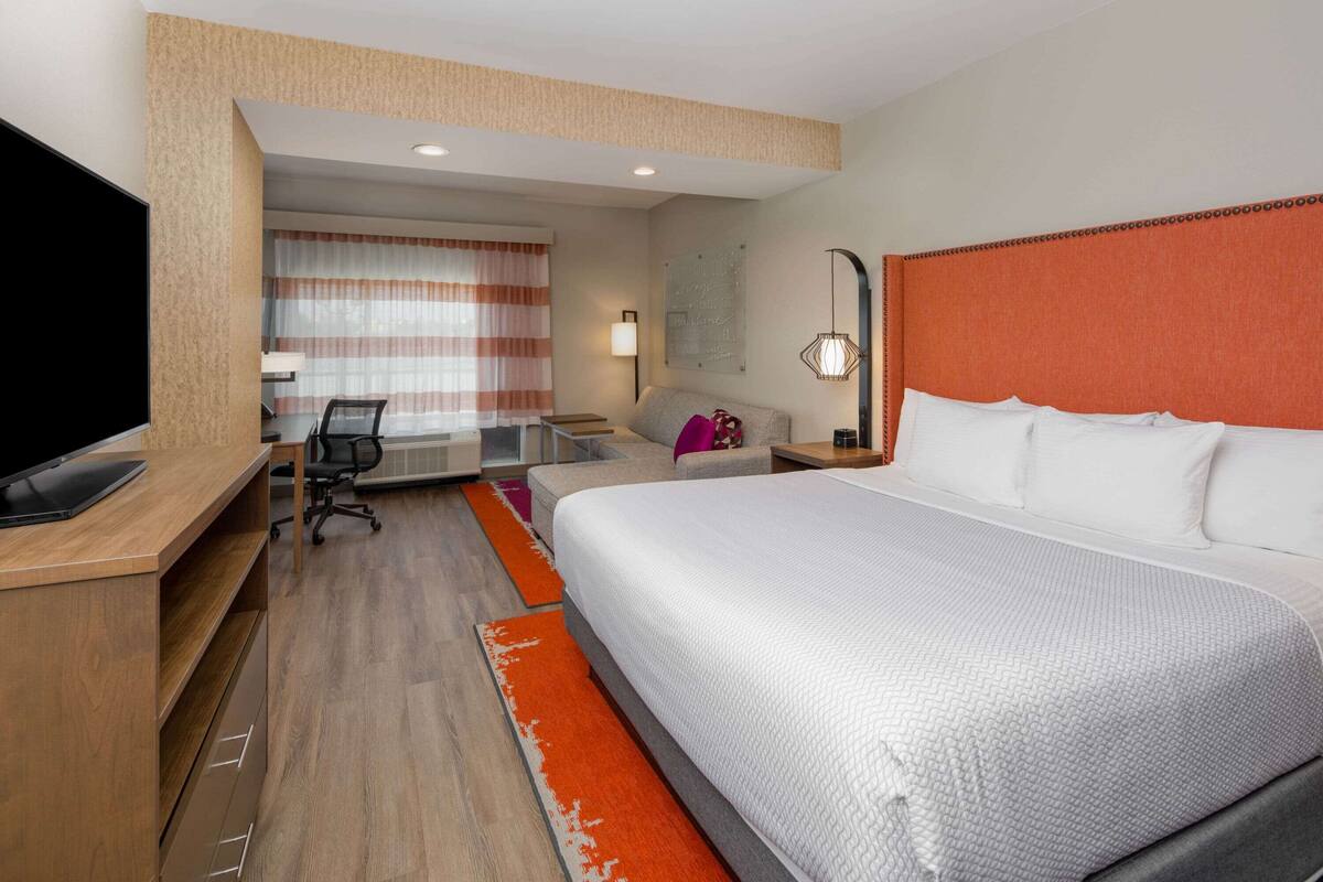 A hotel room with a large bed, a desk with a TV, a chair, and a window with curtains.