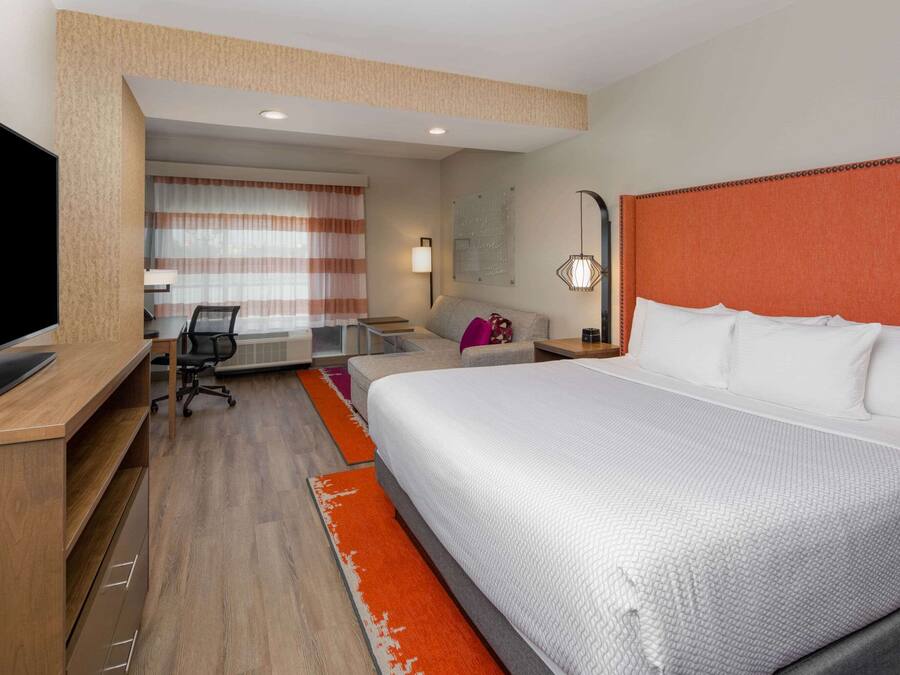 Habitación de hotel con una cama grande, un escritorio con televisor, una silla y una ventana con cortinas.