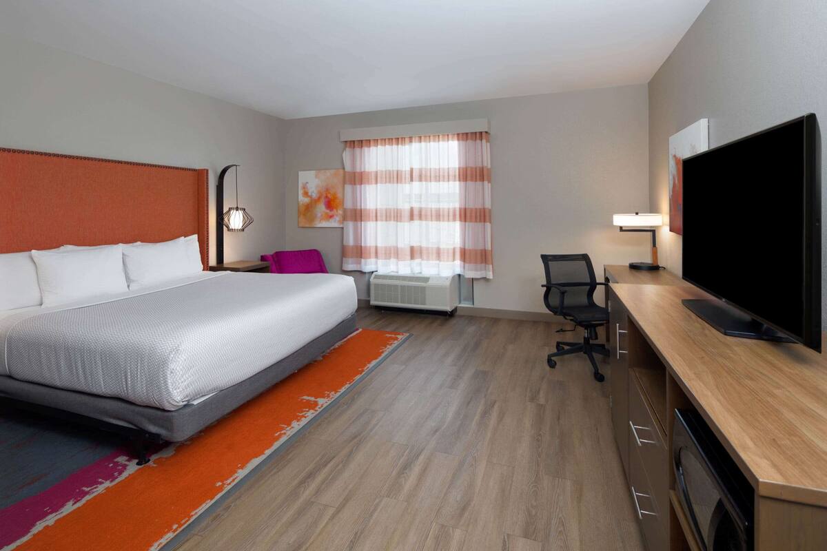 A hotel room with a bed, desk, chair, TV, and a window with curtains.