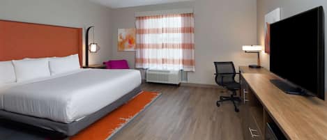 Una habitación de hotel con cama, escritorio, silla, televisor y ventana con cortinas.