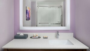 A bathroom with a large mirror, a white sink, and a glass shower enclosure.