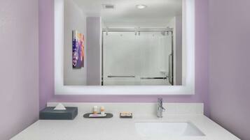 Un baño con un espejo grande, un lavamanos blanco y una cabina de ducha de vidrio.