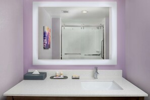 A bathroom with a large mirror, a white sink, and a glass shower enclosure.