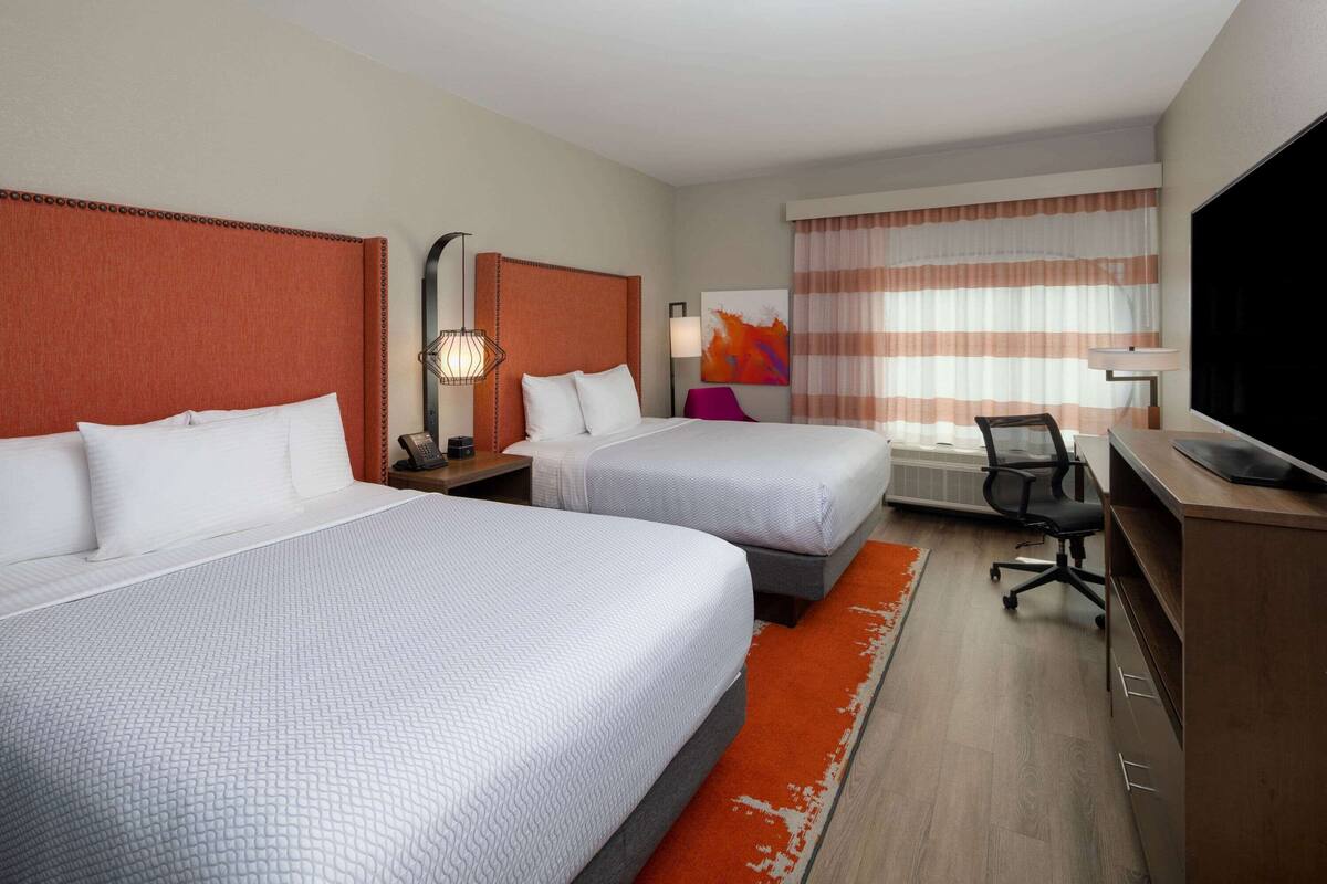 A hotel room with two beds, a desk, a chair, and a television.