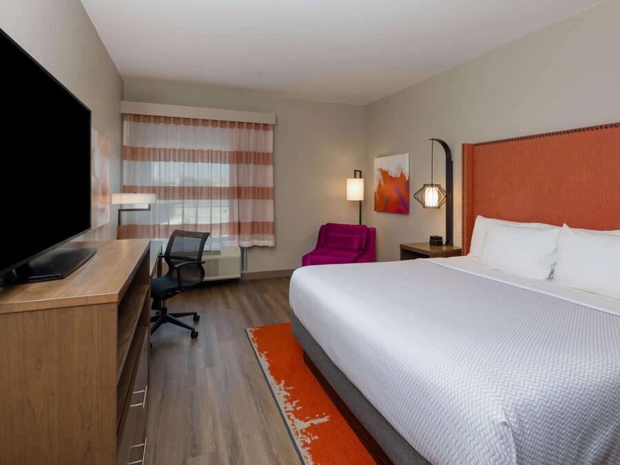 Hotelkamer met een groot bed, een bureau, een flatscreen televisie, een stoel en een raam met gordijnen.