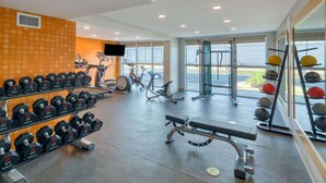 Une salle de sport équipée de divers appareils, notamment des haltères, des tapis de course et des ballons d’exercice.