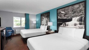A hotel room with two beds, a desk, a chair, and a large window.