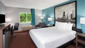 Habitación de hotel con una cama grande, un escritorio con computadora, una silla y un ventanal con cortinas.