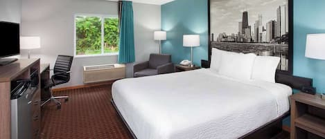 Habitación de hotel con una cama grande, un escritorio con computadora, una silla y un ventanal con cortinas.