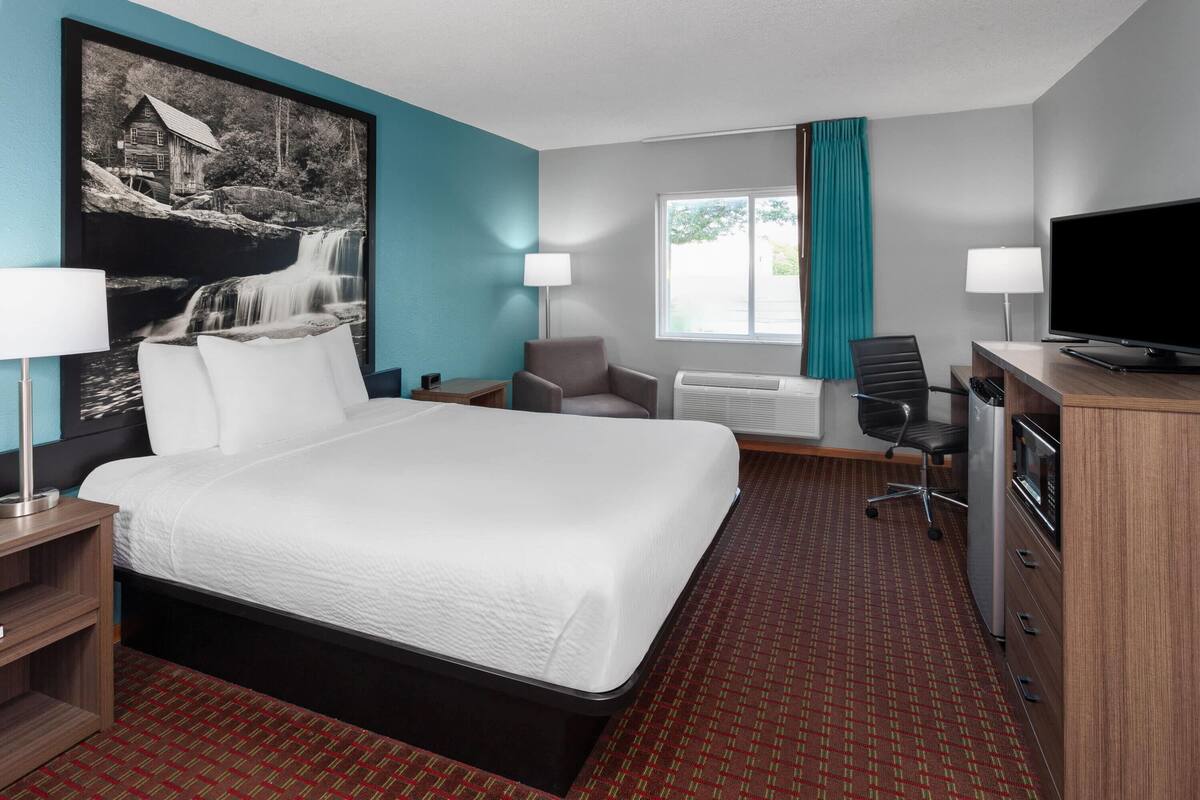 Quarto de hotel com uma cama grande, uma escrivaninha, uma cadeira, uma televisão e uma janela com cortinas.