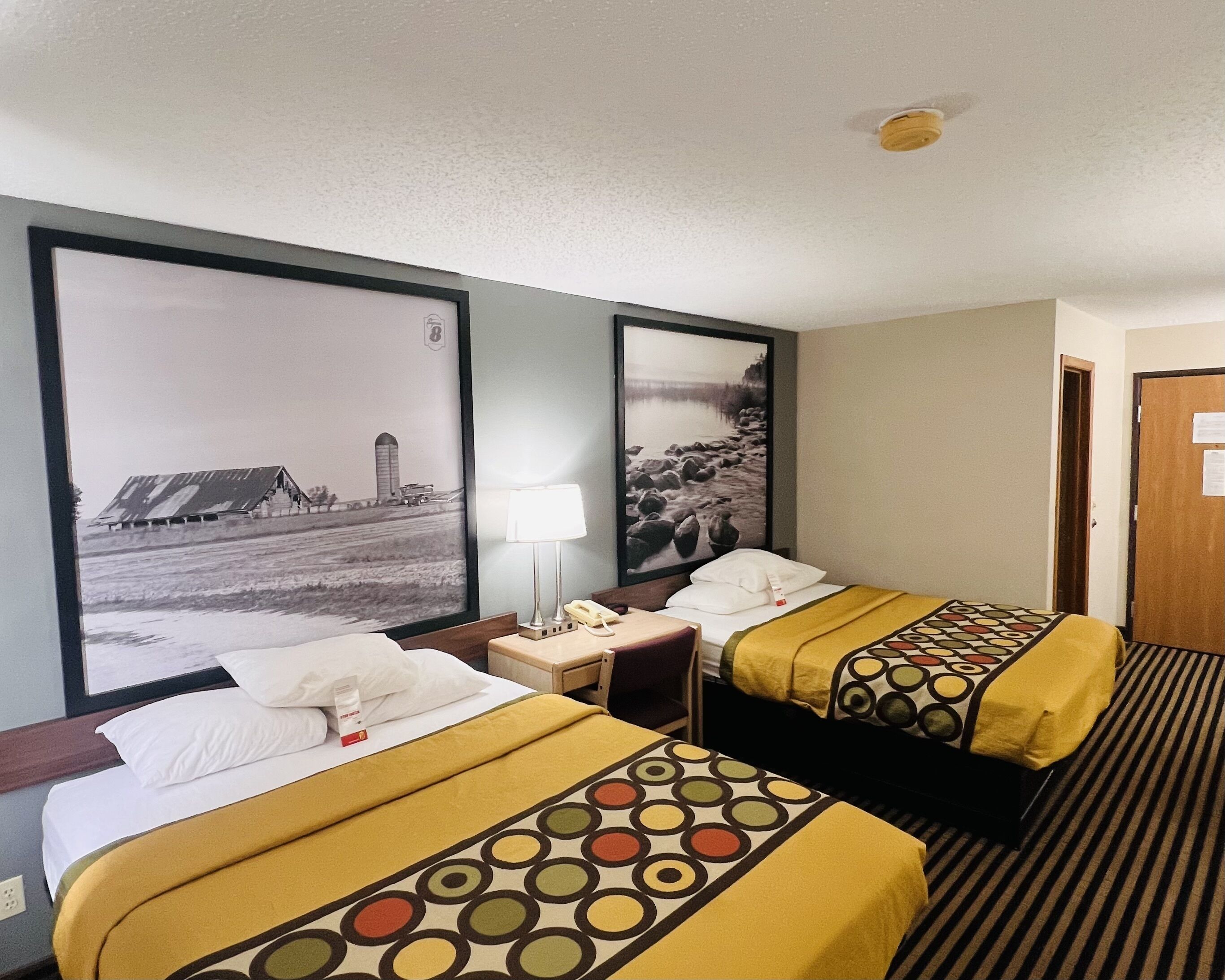 Ein Hotelzimmer mit zwei Betten, einem Nachttisch mit Lampe, einem Telefon und einem gerahmten Bild an der Wand.