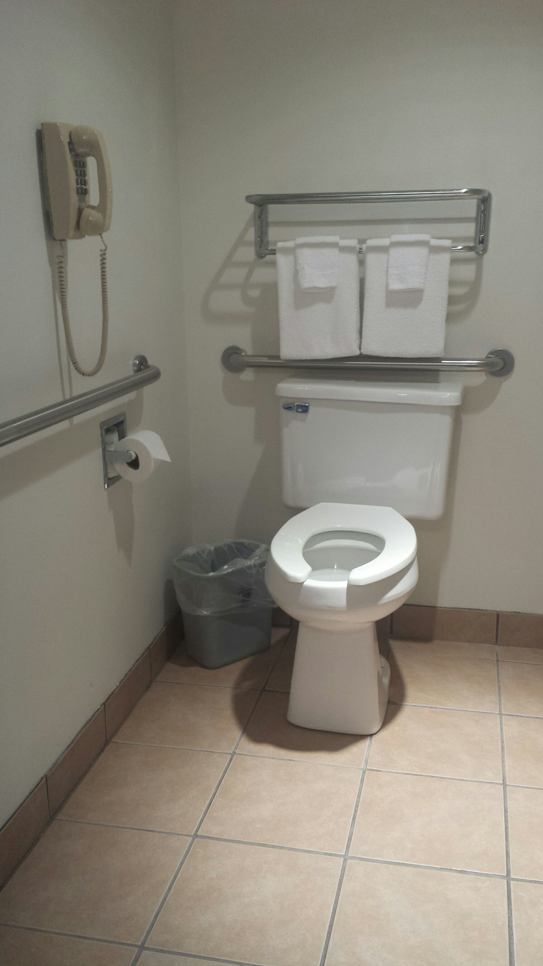 Um banheiro pequeno com vaso sanitário, secador de mãos, lixeira e telefone fixado na parede.