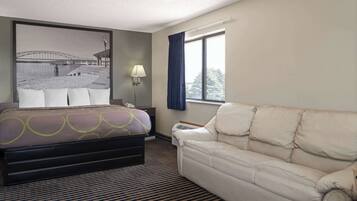 Habitación de hotel con cama, sofá, ventana grande, lámpara y aire acondicionado instalado en la pared.