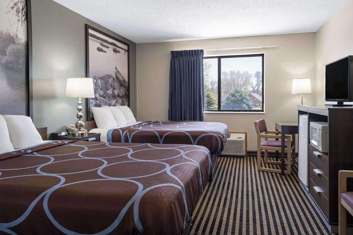 A hotel room with two beds, a desk, a television, and a window with curtains.