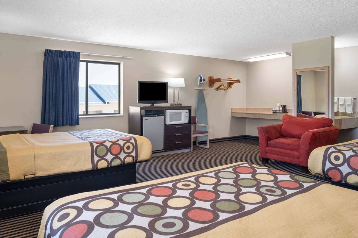 A hotel room with two beds, a desk with a TV, a chair, a microwave, and a large mirror.