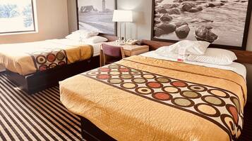 A hotel room with two beds, a bedside table with a lamp, and a large framed picture on the wall.