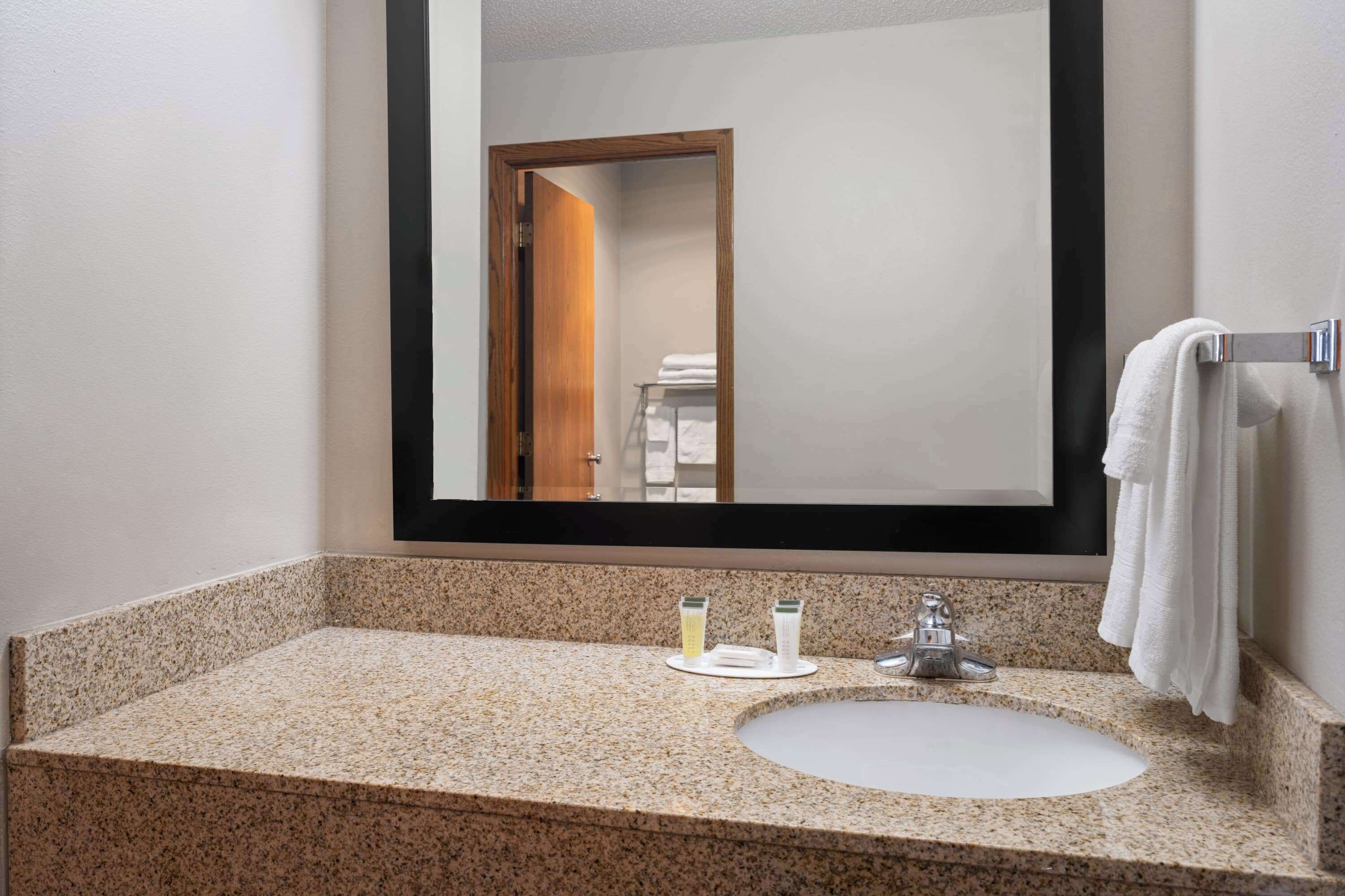 Une salle de bain avec un comptoir en granit, un lavabo, un miroir et un porte-serviettes.