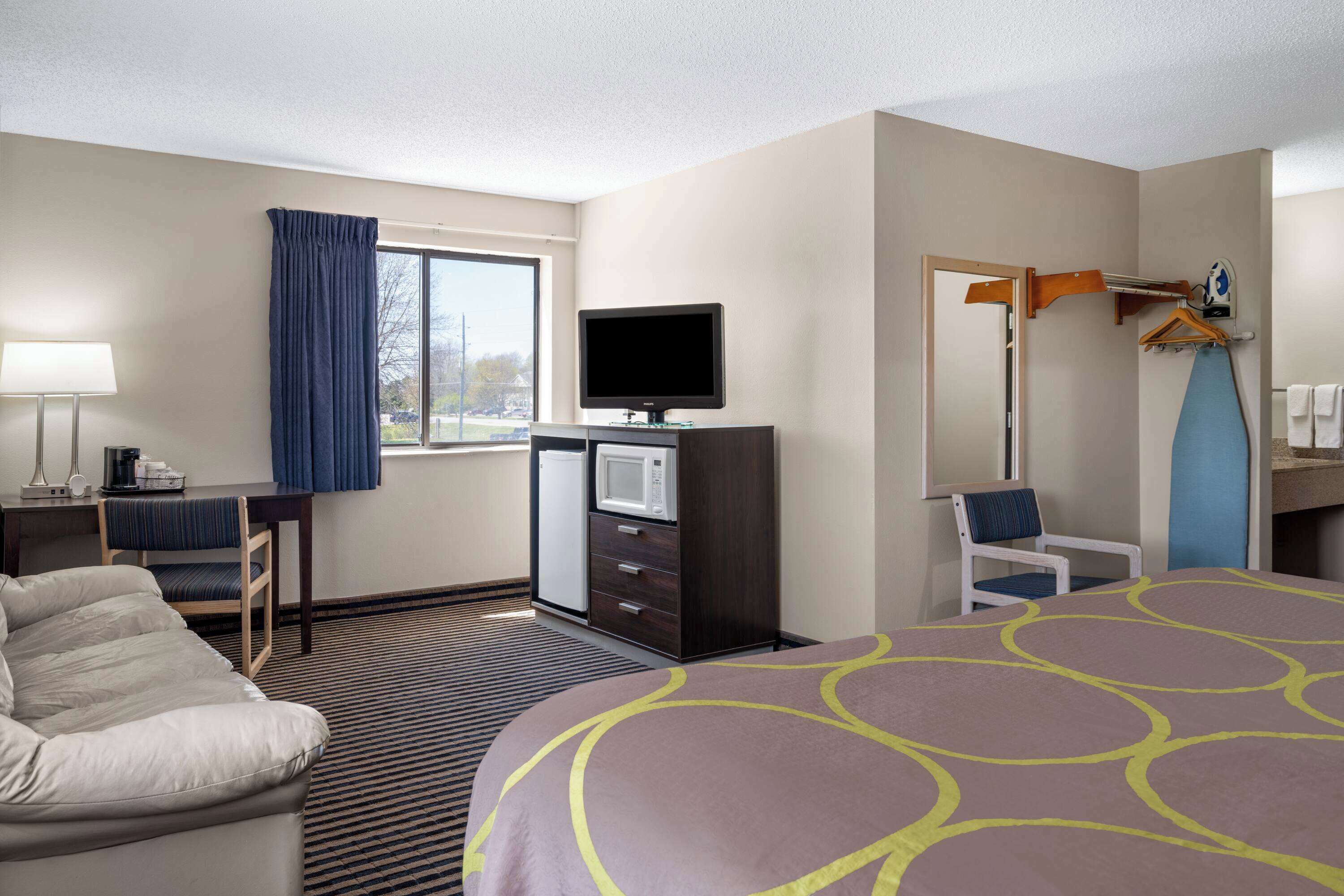 A hotel room with a bed, a desk with a computer, a microwave, a chair, and a TV.