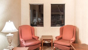 Una habitación con dos sillones tapizados de rojo, una mesita de madera, una lámpara blanca y dos cuadros en la pared.