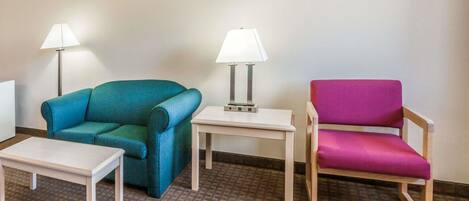Ein Zimmer mit einem türkisfarbenen Sessel, einem kleinen weißen Tisch, einem kleinen weißen Tisch mit Lampe und einem pinkfarbenen Sessel.