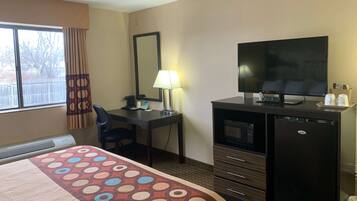 Een hotelkamer met een bed, bureau, televisie, koelkast en een raam met gordijnen.