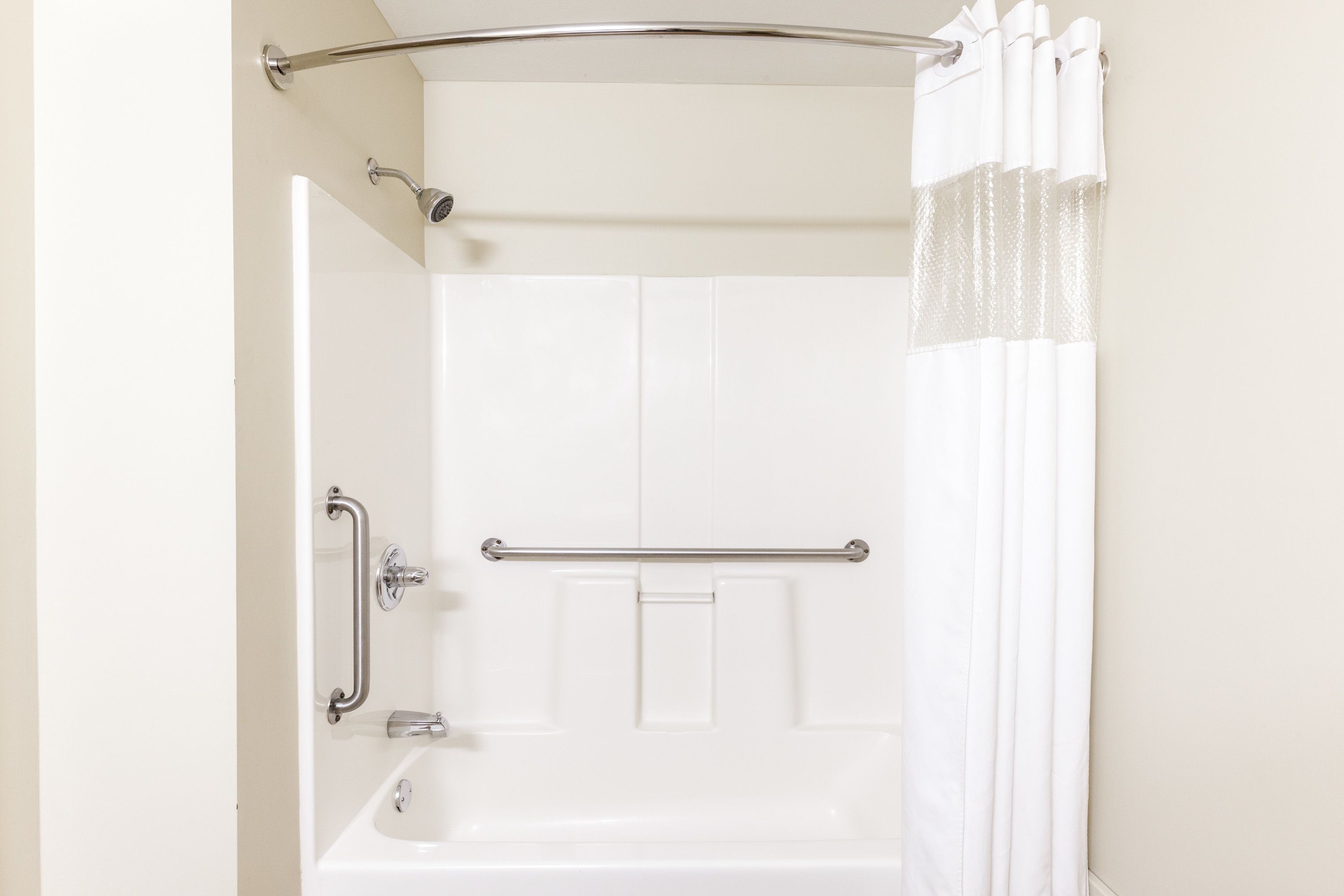 Une salle de bain avec une baignoire blanche, une douche dotée d’une porte en verre et une barre d’appui.